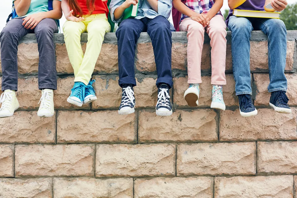 Schulkinder sitzen mit bunten Sneakern auf einer Mauer